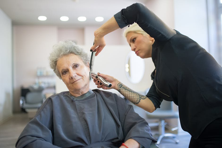 Elderly woman receiving a haircut from a stylist using clippers in a hair salon.