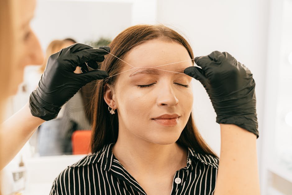 A woman receives precise eyebrow threading in a modern salon setting.